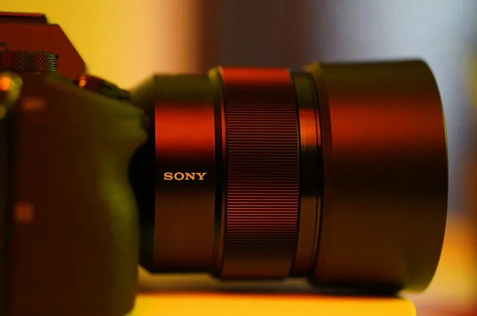 Close-up of a Sony camera body and large Sony lens in warm amber and red light.